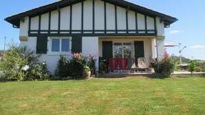 A two-story building with a gabled roof, a front porch with red chairs, and a small garden with potted plants and flowers. - House / Villa - Saint Pée sur Nivelle (Saint-Pée-Sur-Nivelle)