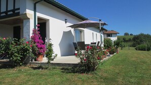 A white building with a green roof, a patio with outdoor furniture, and a garden with pink flowers. - House / Villa - Saint Pée sur Nivelle (Saint-Pée-Sur-Nivelle)