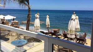 Una terraza frente a la playa con mesas al aire libre, sombrillas y vistas al mar.