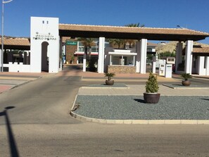 A gated entrance with a sign for 'URBANIZACION PUEBLO SALINAS' and a covered area with planters.