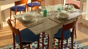 A dining area with a table set for four, chairs with blue cushions, a tiled floor, and a view of the sea through a balcony. - confortable cottage with stunning seaview and total privacy in the nature (Montemarcello-Ameglia (SP))