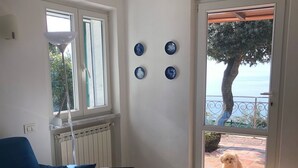 A living room with a blue sofa, a small table, and a view of a dog outside through a glass door. - confortable cottage with stunning seaview and total privacy in the nature (Montemarcello-Ameglia (SP))