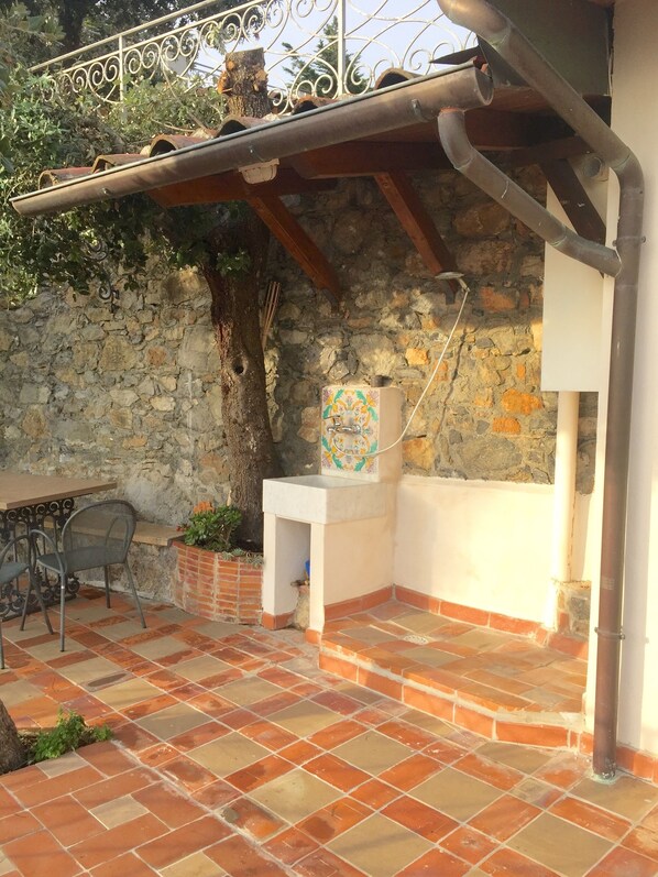 A rustic outdoor area with a stone wall, a metal table with chairs, a small white sink, and a tree. - confortable cottage with stunning seaview and total privacy in the nature (Montemarcello-Ameglia (SP))