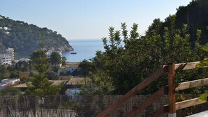 A coastal view with a wooden staircase leading down to a beach, surrounded by greenery and buildings.