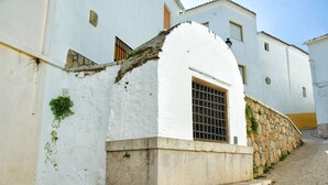 Un edificio blanco con base de piedra, una ventana con reja de metal y un pequeño tramo de escalones que conducen a la entrada.