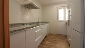 Una cocina con gabinetes blancos, encimera de granito, pileta de acero inoxidable y horno empotrado.
