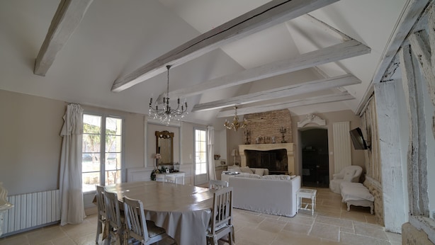 A spacious dining area with a large round table, white chairs, and a chandelier. There is a fireplace and a cozy seating area with sofas and a small table. - CHARMING PERIGOURDINE ALONG THE DORDOGNE (Cours-De-Pile)