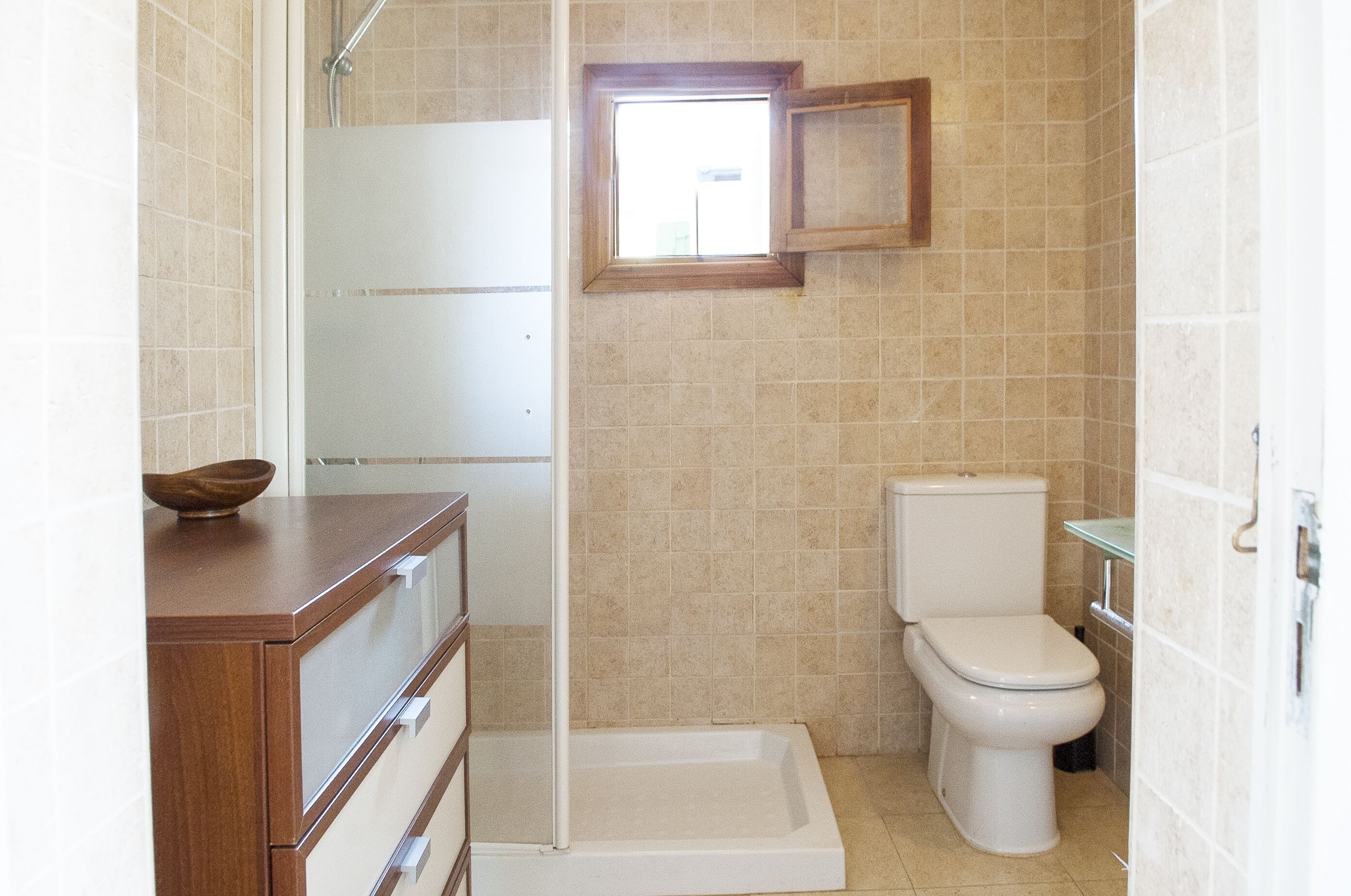 A bathroom with a shower, toilet, and a wooden vanity.
