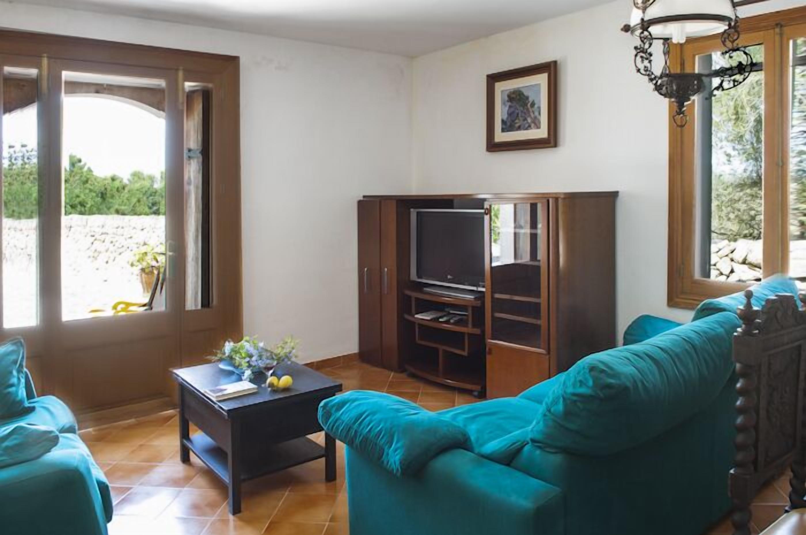 Een woonkamer met een blauwgroene bank, een donker houten entertainmentkast en een televisie.