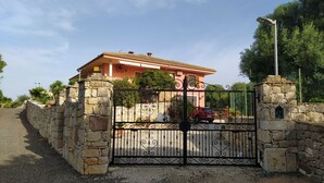 Une maison rose avec un portail en pierre et une voiture rouge garée devant.