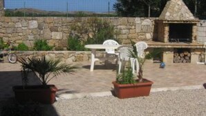 Une terrasse extérieure avec des murs en pierre, une cheminée en pierre et des chaises en plastique blanches.