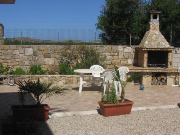 An outdoor patio with stone walls, a stone fireplace, and white plastic chairs.