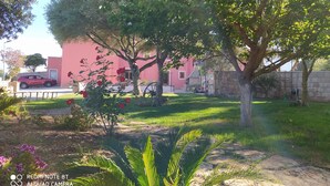 Un jardin avec un bâtiment rouge, un arbre et une voiture garée.