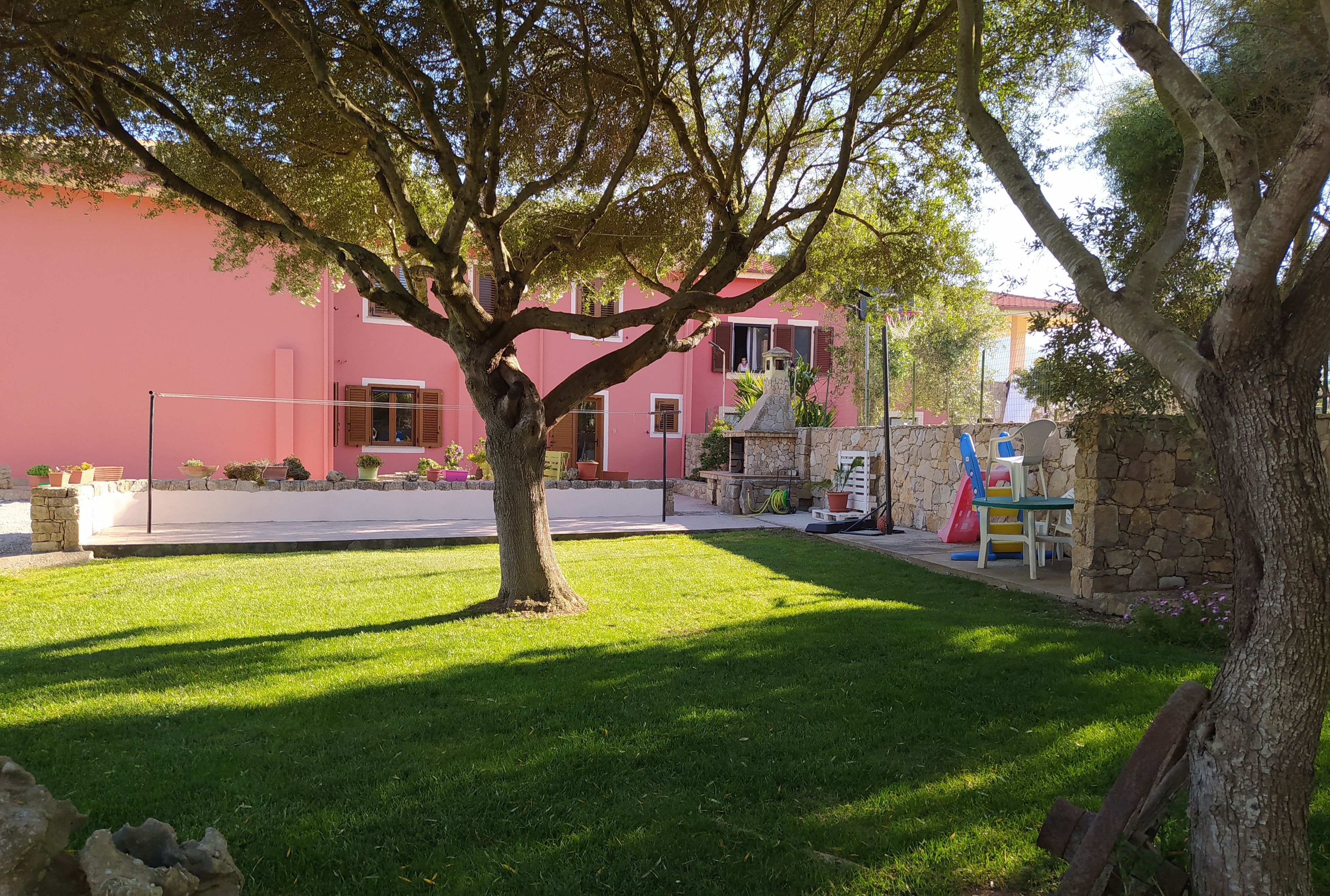 Un edificio rosa con un muro in pietra, un prato verdeggiante e un albero.
