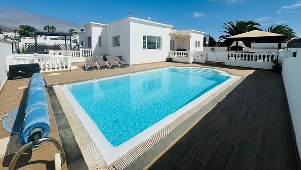A rooftop swimming pool with a clear blue pool, white walls, and a wooden deck.