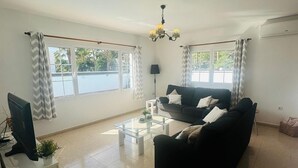 A spacious living room with a black sofa, a glass coffee table, and a TV on a stand.