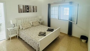 A bedroom with a bed, bedside tables, a ceiling light, and an air conditioning unit.