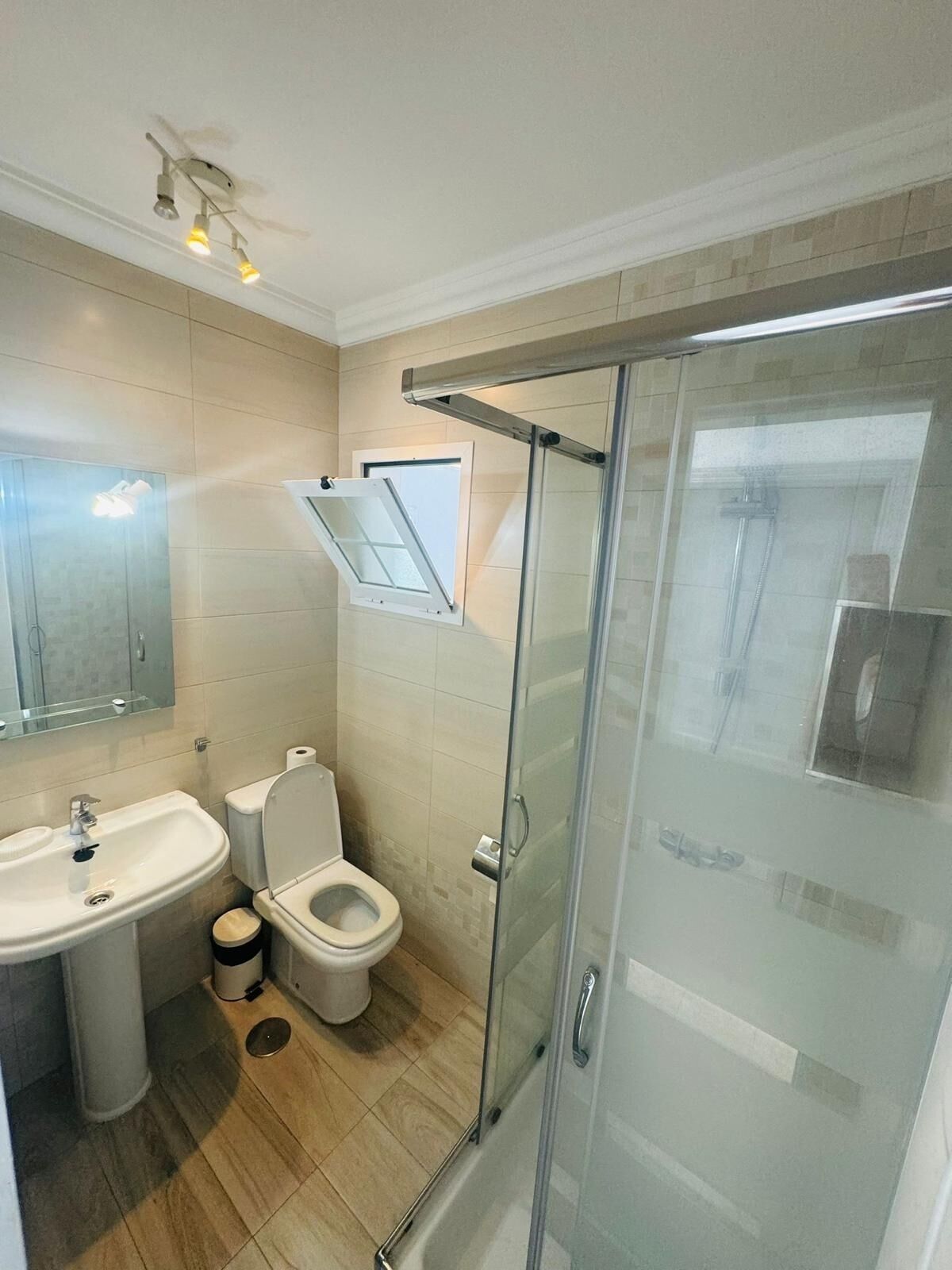 Un baño moderno con cabina de ducha de vidrio, lavamanos pedestal y retrete.