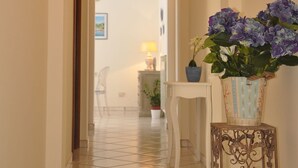 A hallway with a tiled floor, white walls, and an arched doorway leading to another room. There is a small table with a potted plant and a vase with flowers. - L'Ancora - Bright Sea front, Self Catering Apartment (Minori)