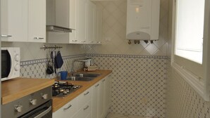 A kitchen with white cabinets, a wooden countertop, a gas stove, an oven, a hanging light fixture, and a window. - L'Ancora - Bright Sea front, Self Catering Apartment (Minori)