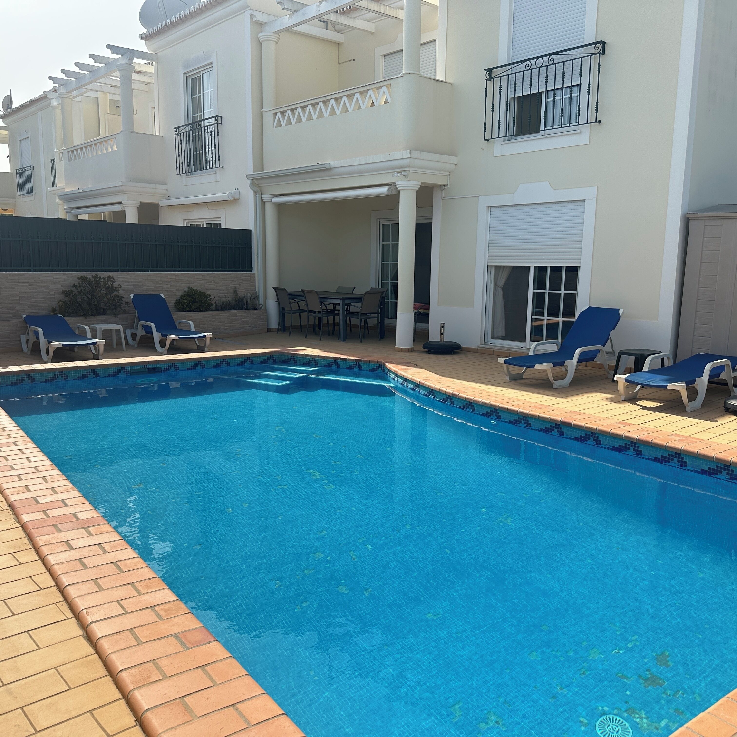 A swimming pool with lounge chairs, a covered patio area, and a building with balconies.