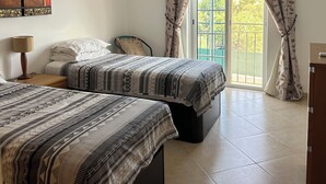A bedroom with two beds, a nightstand, a lamp, a window with curtains, and a painting on the wall. - Impressive Villa in Ferragudo, with Private Pool, Air Con, Garden & Fibre WiFi. (lagoa)
