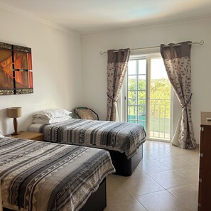 A bedroom with two beds, a nightstand, a lamp, a window with curtains, and a painting on the wall. - Impressive Villa in Ferragudo, with Private Pool, Air Con, Garden & Fibre WiFi. (lagoa)