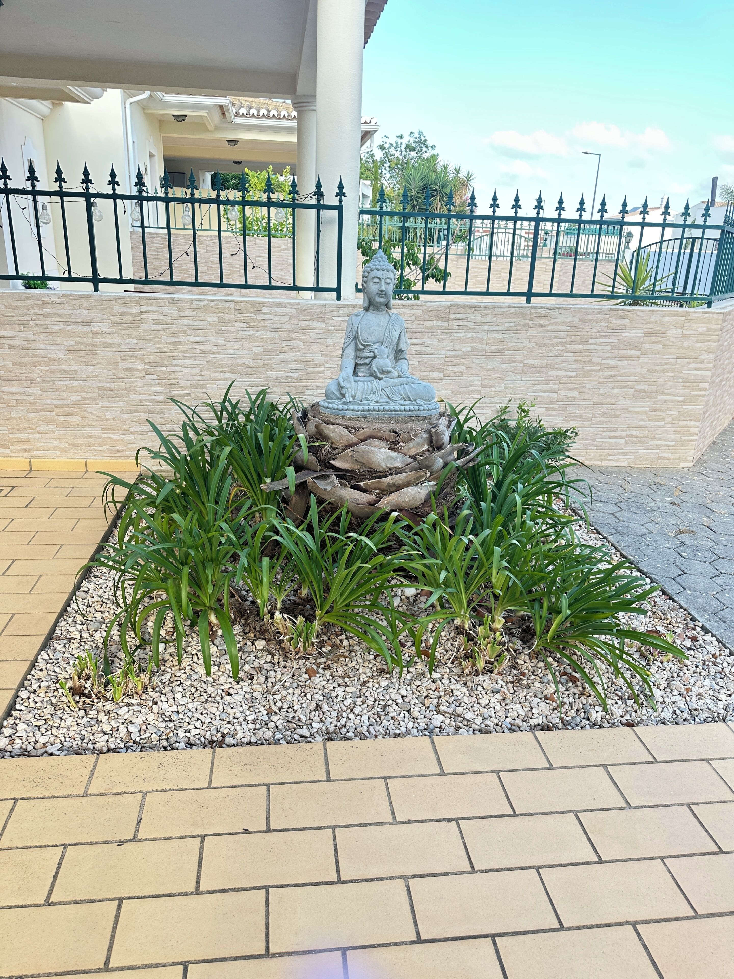 Una estatua de Buda de piedra rodeada de plantas sobre una superficie pavimentada.