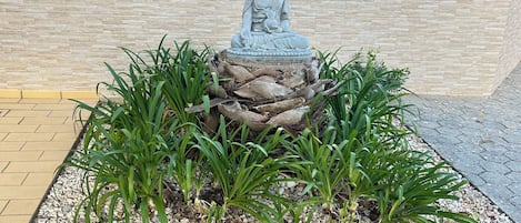 Una estatua de Buda de piedra rodeada de plantas sobre una superficie pavimentada.