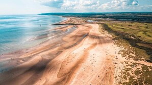 An aerial view of a coastal landscape with a beach, dunes, and a distant shoreline. - Beautiful Seaside Cottage 1 minute from the beach - The Tides (Camber)