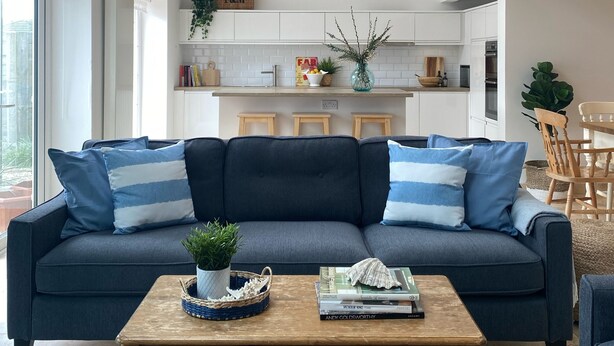 A living room with a dark blue sofa, wooden coffee table, and a bookshelf. - Beautiful Seaside Cottage 1 minute from the beach - The Tides (Camber)