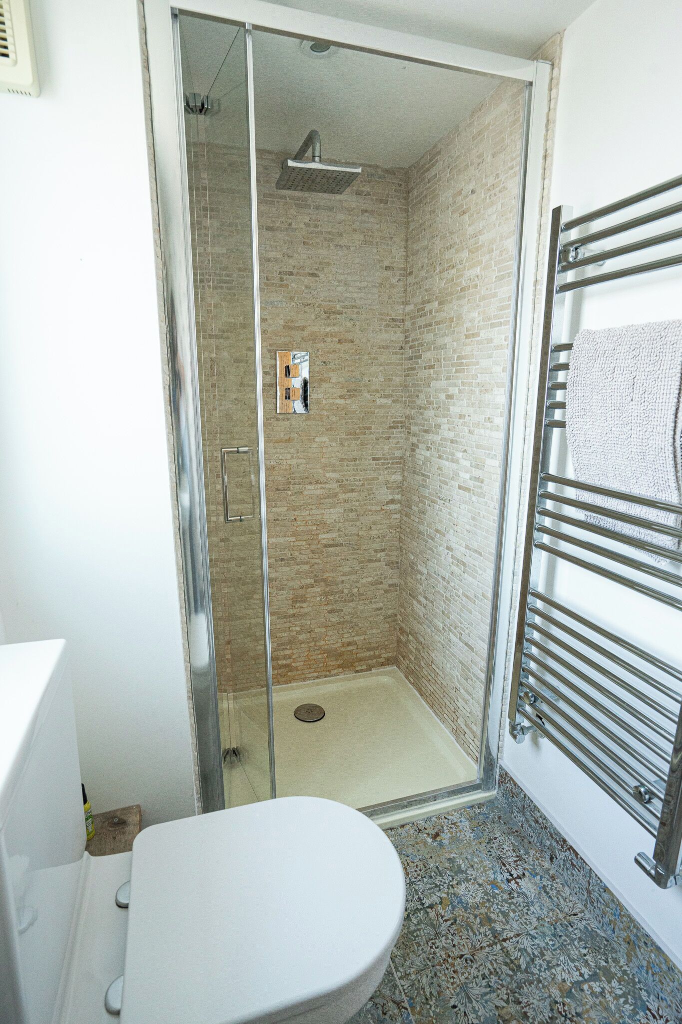 A bathroom with a glass-enclosed shower, a white toilet, and a towel rack with a towel.