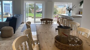 Een ruime woonkamer met een houten eettafel, stoelen en een groot raam met uitzicht op een tuin.