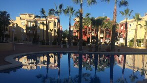 A pool with clear reflections of palm trees and buildings, surrounded by a paved area with steps leading into the water. - Puerto Marina 2 bedroom 2 bath apartment in Los Alcazares (Murcia)