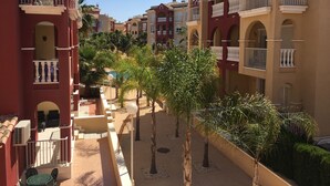 A courtyard with red and beige buildings, balconies, and palm trees. - Puerto Marina 2 bedroom 2 bath apartment in Los Alcazares (Murcia)
