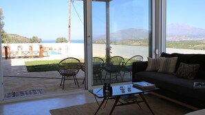 A modern living room with a glass door leading to an outdoor patio. Inside, there is a sofa, a coffee table, and several chairs. - Villa in Kamilari, Heraklion and surroundings sea and mountain view and private swimming pool (Kamilari)