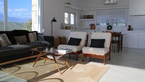 A modern living room with a sofa, chairs, and a coffee table. There is a view of mountains through large windows. - Villa in Kamilari, Heraklion and surroundings sea and mountain view and private swimming pool (Kamilari)
