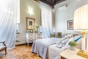 Ein Schlafzimmer mit Bett, Schminktisch, Lampe und einem Fenster mit Vorhängen.