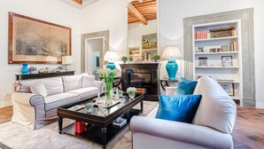 Una sala de estar con chimenea, un conjunto de sofás, una mesa de centro y una estantería.