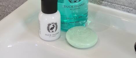 Un lavabo de salle de bain avec un flacon de savon pour les mains de la marque Duck Island, un flacon-pompe et un pain de savon.