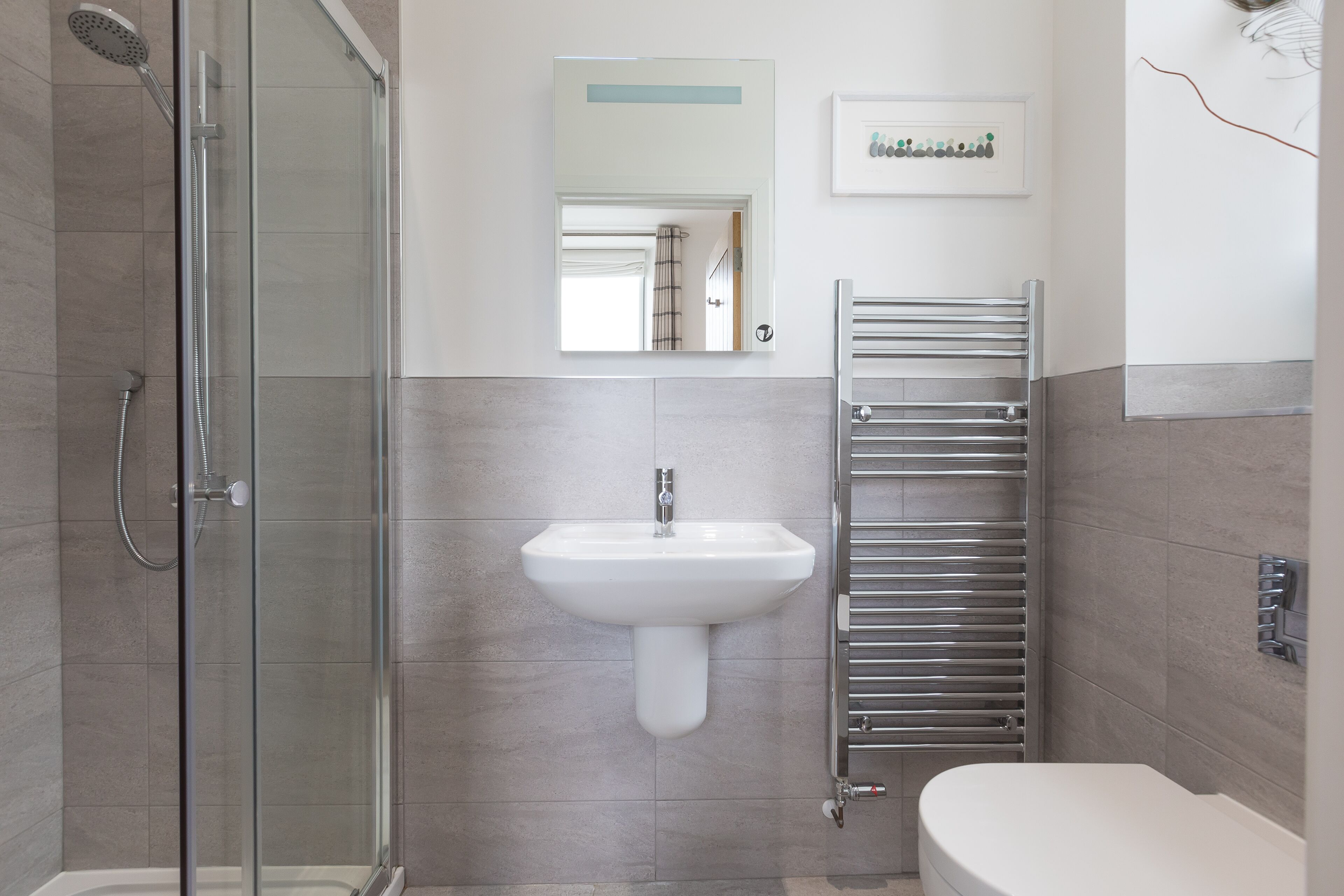 Une salle de bain moderne dotée d’une douche à parois de verre, d’un lavabo sur colonne et d’un porte-serviettes intégré.