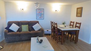 Un salon avec un canapé marron, une table à manger avec des chaises et une table basse blanche.