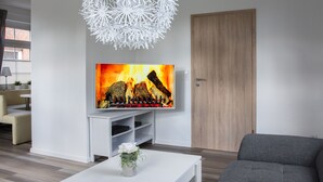Un salon moderne doté d’un téléviseur à écran plat, d’un meuble de rangement blanc, d’un canapé gris et d’un luminaire décoratif blanc en forme de sphère.