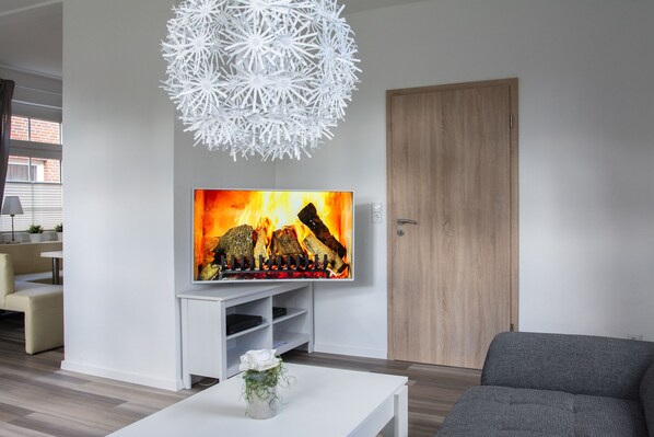 A modern living room with a flat-screen TV, white entertainment unit, grey sofa, and a decorative white spherical light fixture.