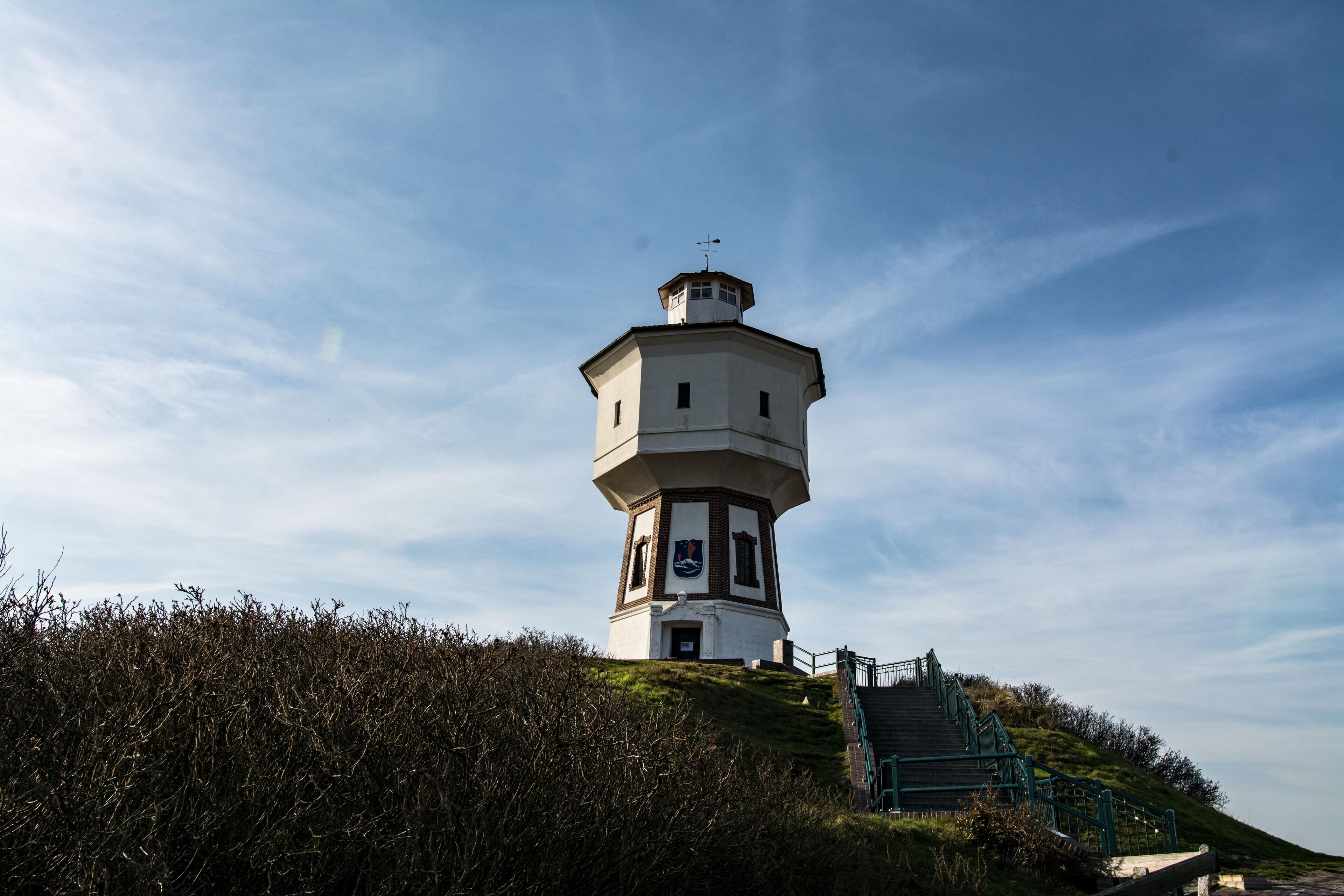 Ein Leuchtturm mit einer Wendeltreppe, die zum Eingang führt, umgeben von dichtem Buschwerk.