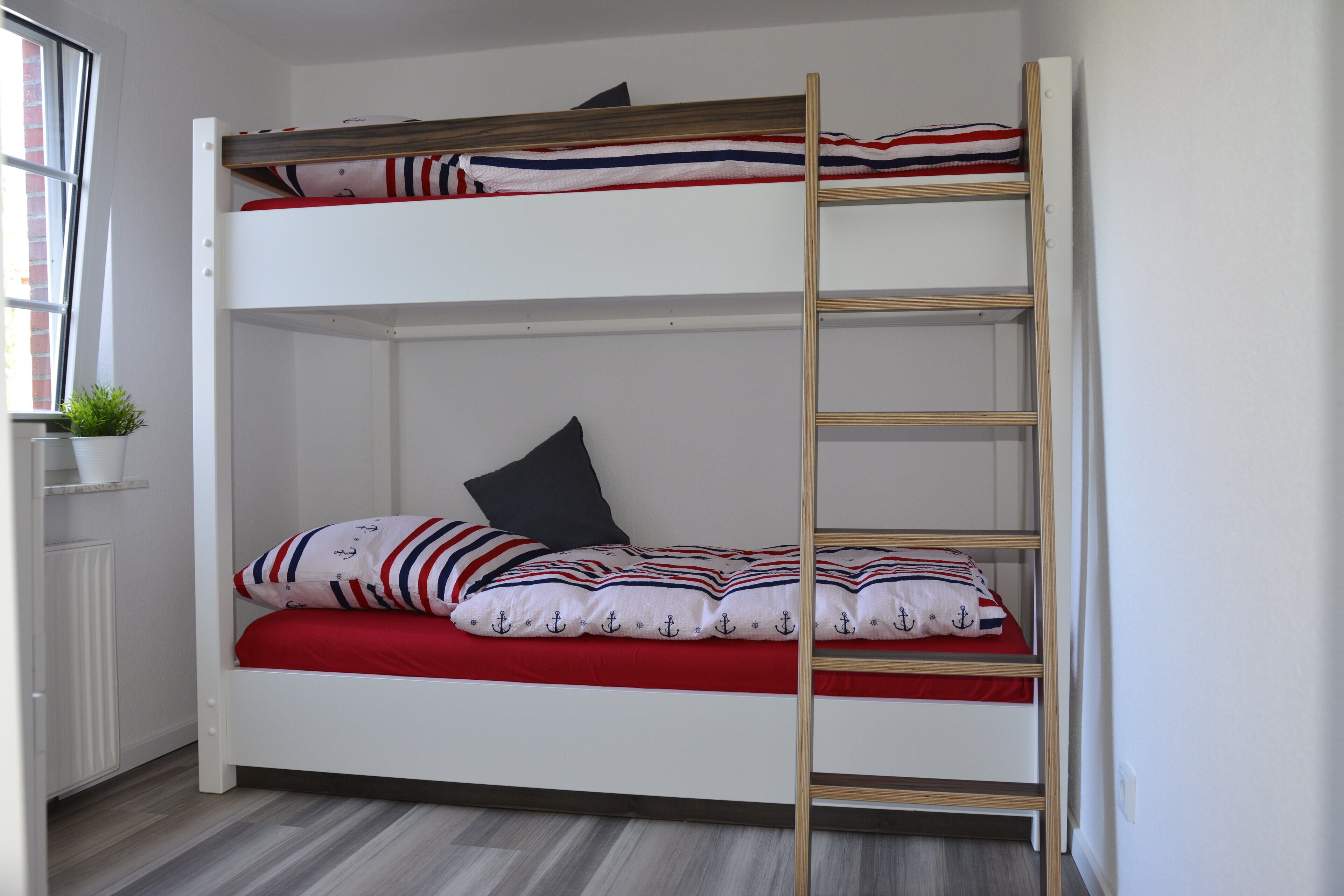 A bunk bed with a ladder, a red mattress, and striped pillows.