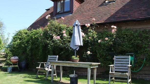 En terrasse med et bord, to stole, grill og haveslange.
