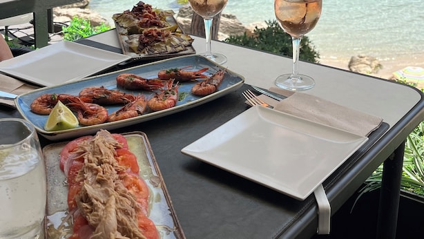 Una mesa dispuesta para una comida con platos de mariscos, copas de vino y vista al mar.