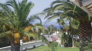 Vista de un patio con palmeras, una cerca blanca y un edificio con un balcón blanco.