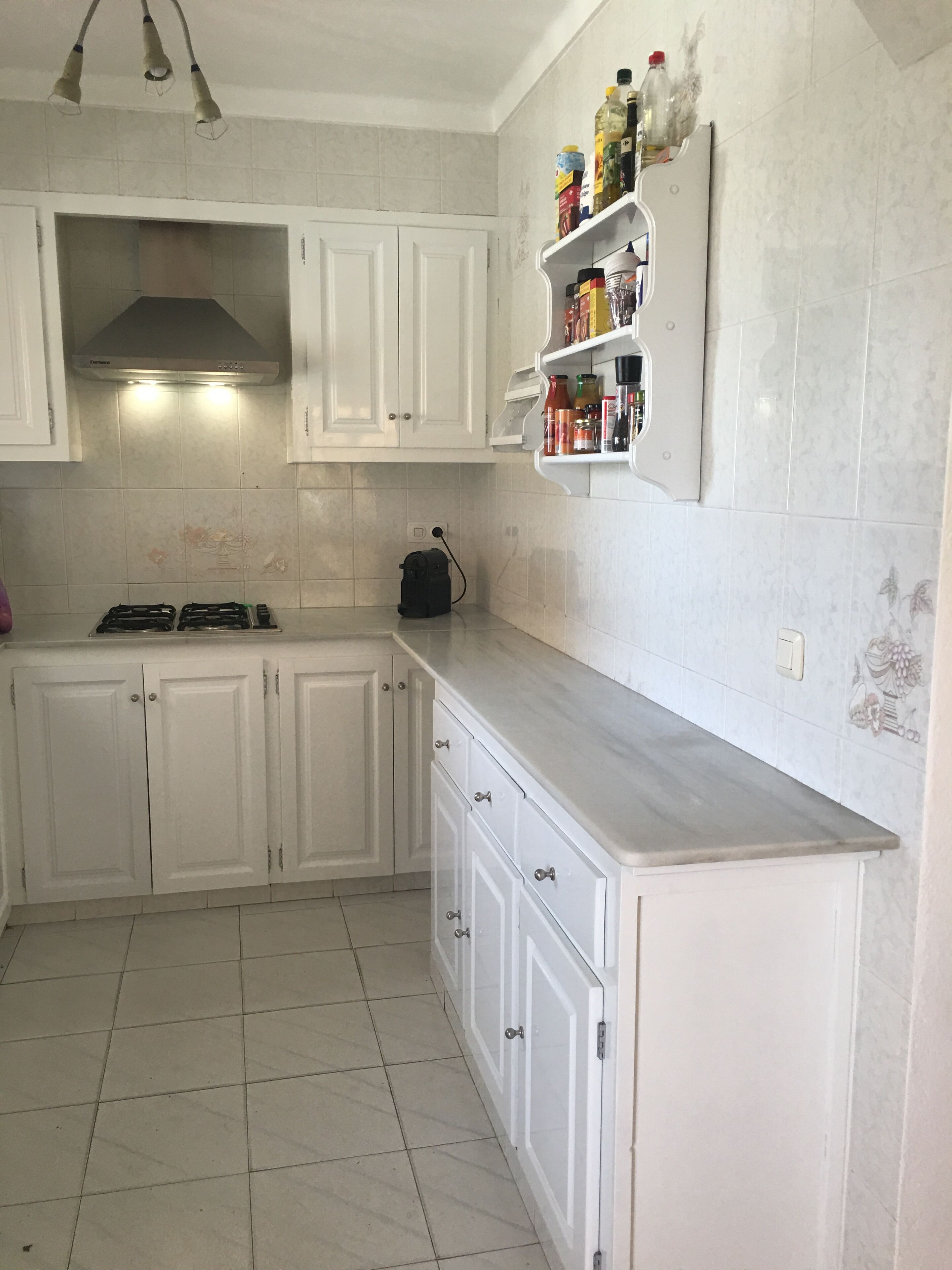 A kitchen with white cabinets, a gas stove, a range hood, a countertop with a coffee maker, and a spice rack.